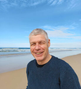 Ian Clark smiling on a beach, with the sea behind him