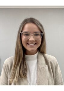 Michaela Hughes wearing glasses, smiling in a portrait