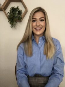 Blair Raatjes smiling, in front of a wall with a hanging plant