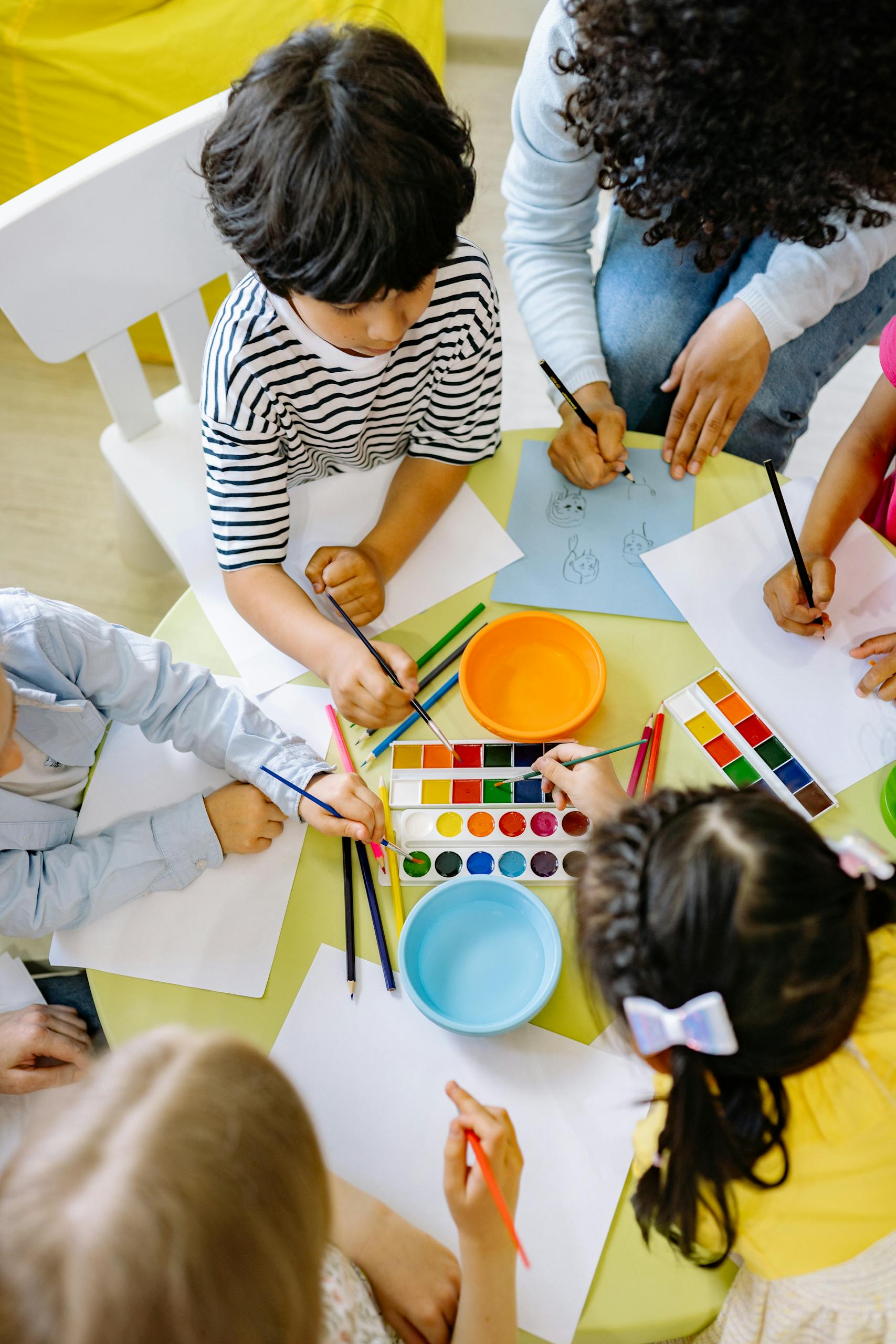 Children painting with watercolours at a preschool art class, seen from above