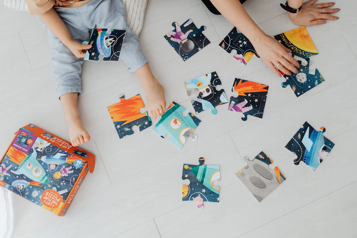 Overhead shot of children solving a colorful space-themed jigsaw puzzle indoors.