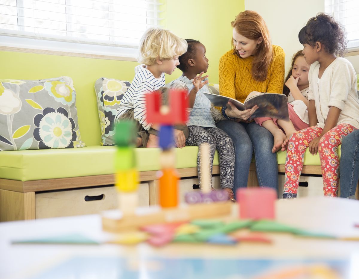 A teacher reading a picture book with a small group of young children on a window seat