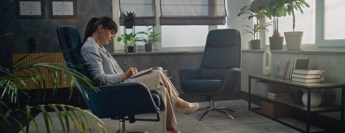 A quiet consulting room with two armchairs and a psychologist making notes