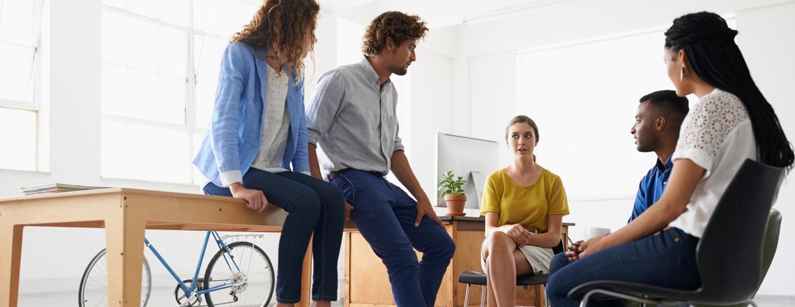 Five colleagues sitting and talking together in a bright open office