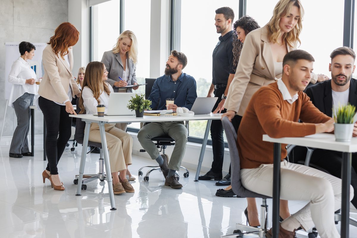 A busy open-plan office with colleagues working at desks and standing in conversation