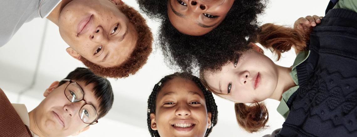 Five teenagers standing in a circle, seen from below, looking down at the camera