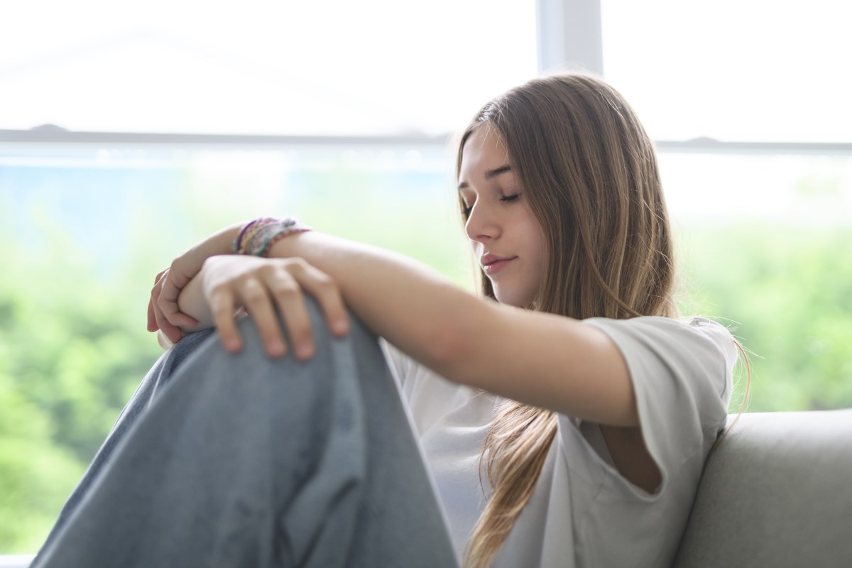 A teenage girl sitting quietly by a window with her arms resting on her knee