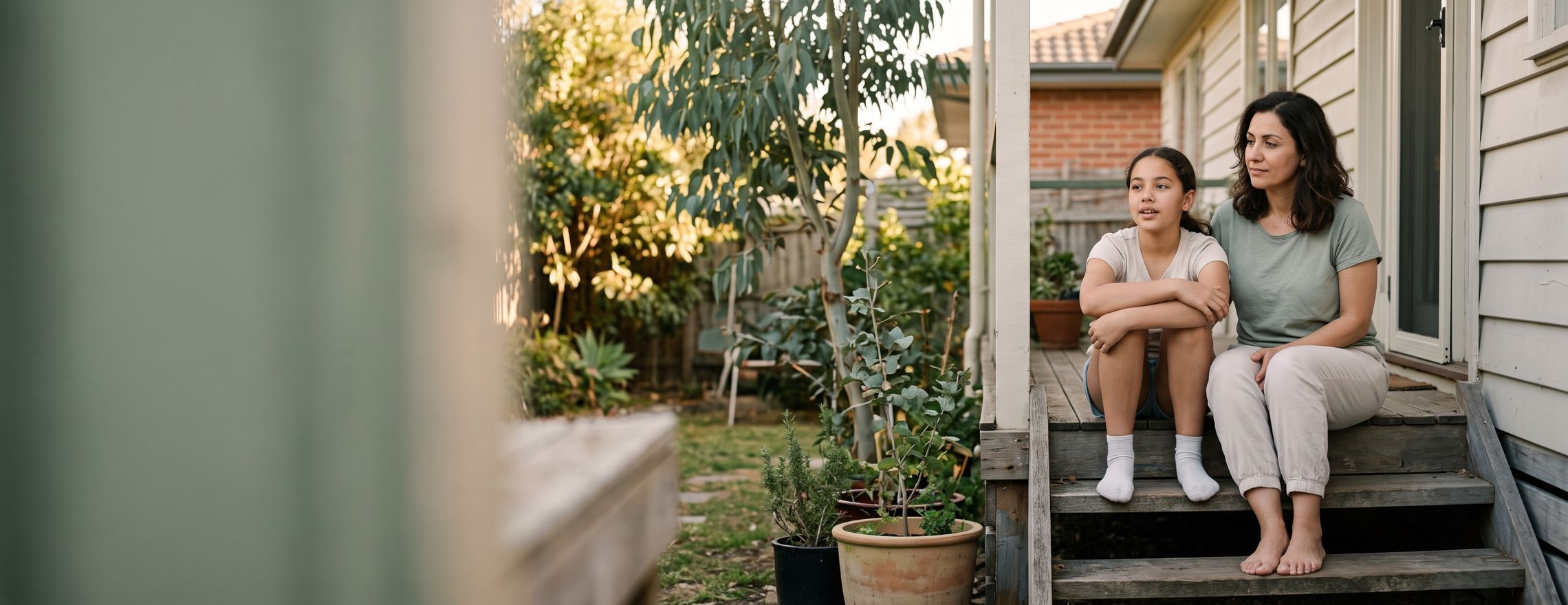 A mother and her teenage daughter sitting side by side on the back steps of a Melbourne home in the late afternoon, talking quietly