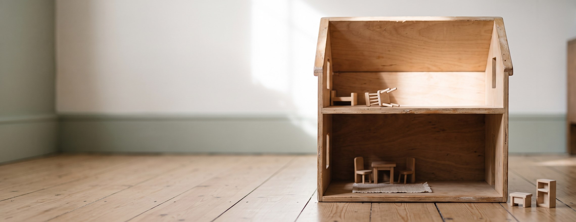 An open wooden dolls house on the floor of a family living room, the lower floor furnished and the upper floor still half empty