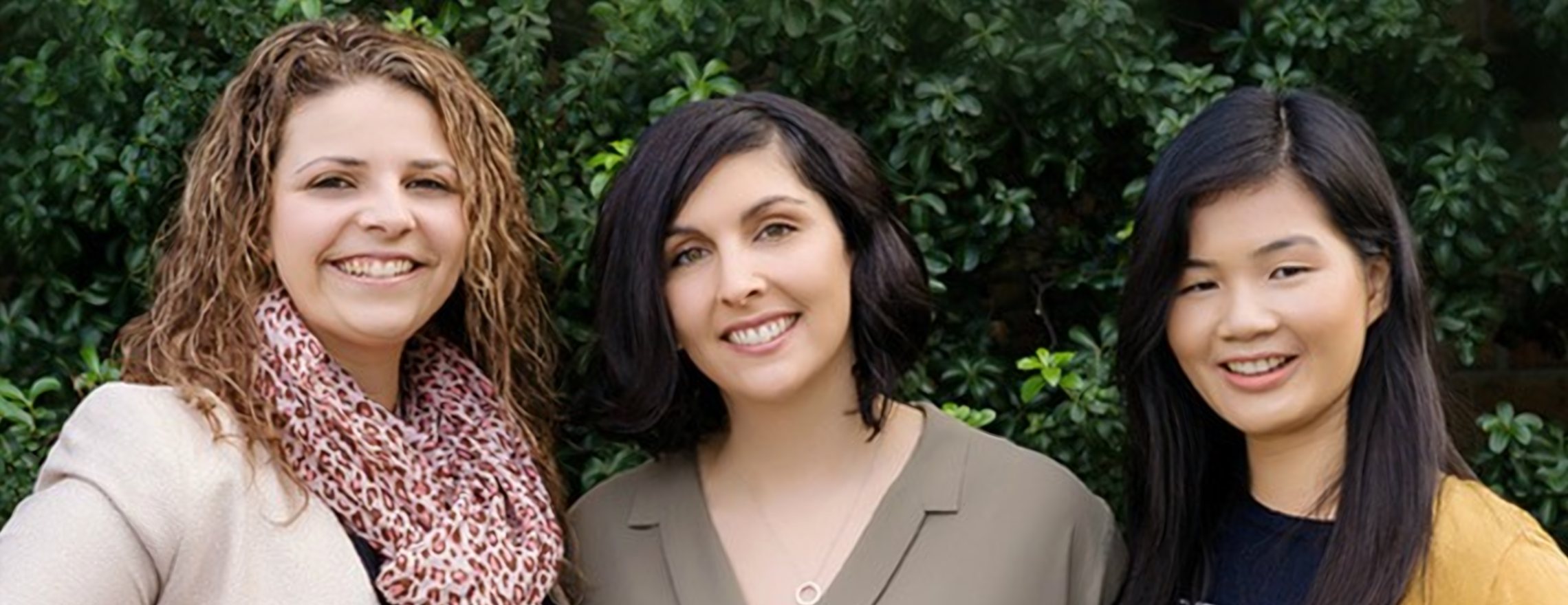 Three smiling psychologists from Your Mind Matters standing together in front of a green hedge