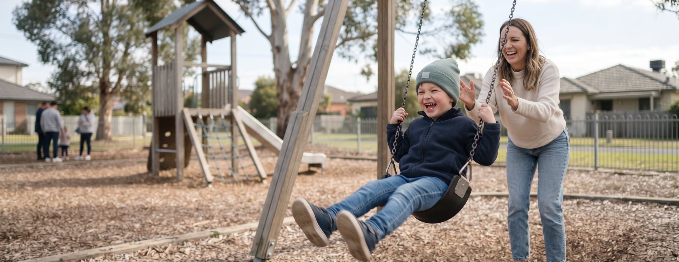Mother laughing as she pushes her young son on a playground swing while he laughs with joy