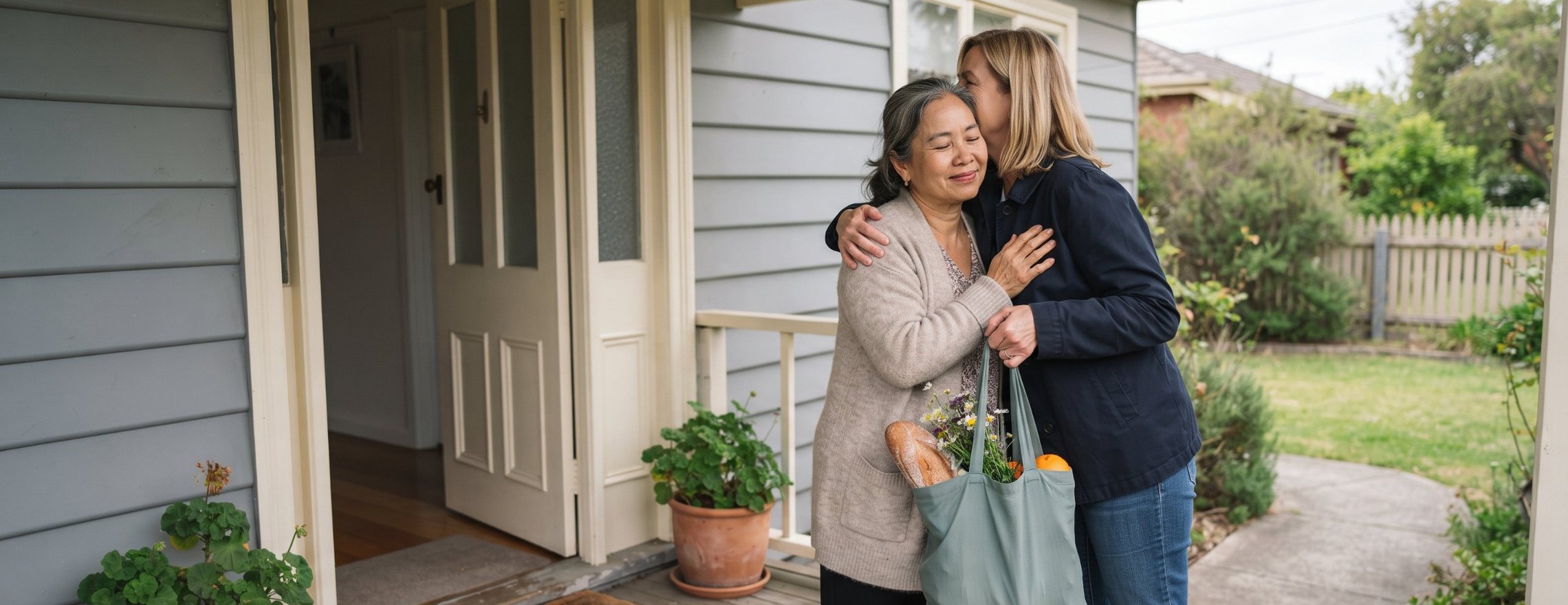 Friend arriving at the front door with a bag of groceries and flowers, sharing a warm hug on the porch